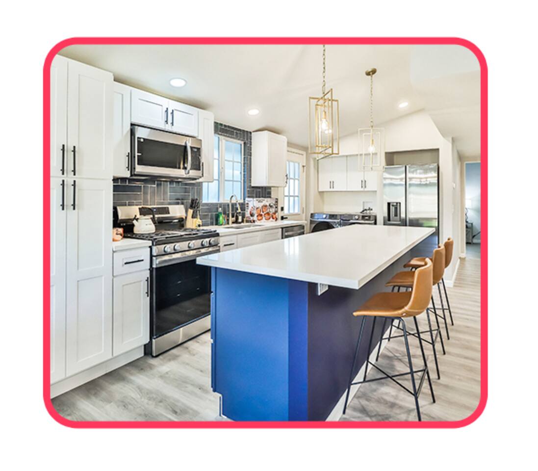 Gourmet kitchen featuring white shaker cabinetry, stainless steel appliances, a large navy blue island with a breakfast bar, and designer pendant lighting.