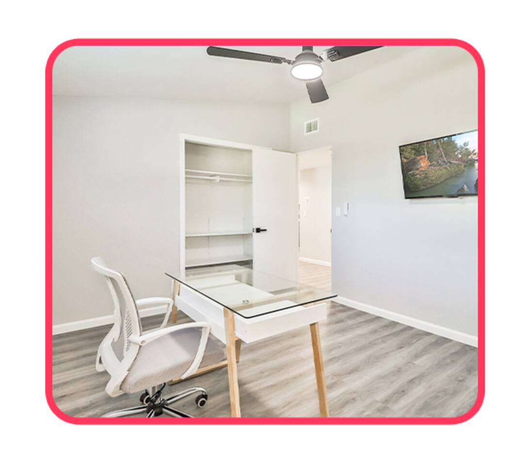Functional office nook featuring a glass-top desk, ergonomic chair, built-in closet shelving, and a wall-mounted TV.
