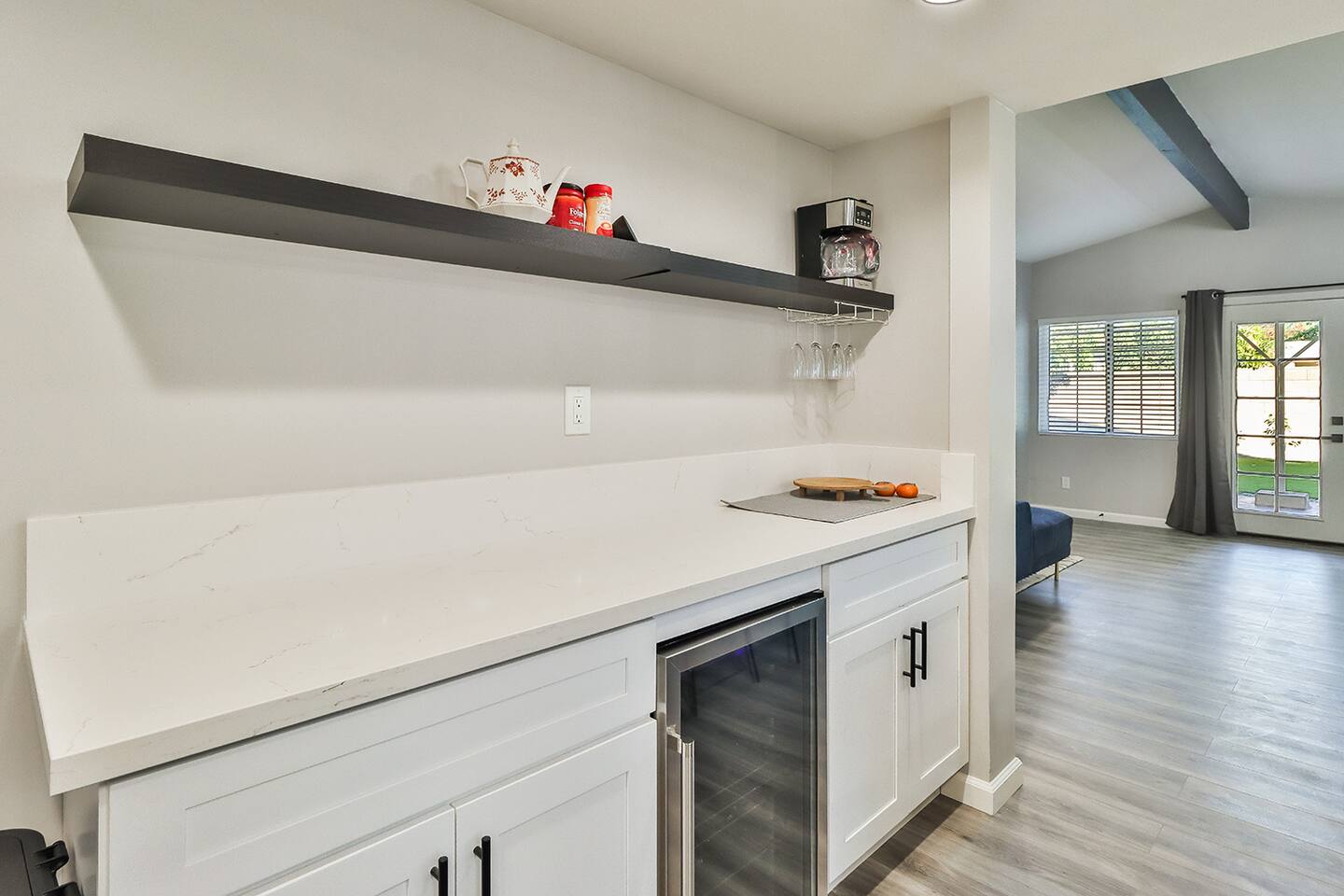 Modern white cabinetry with quartz countertops featuring a built-in wine cooler, floating black shelf, and a secondary view of the gourmet kitchen with a blue subway tile backsplash.