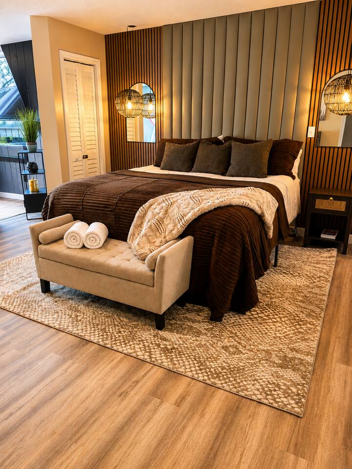 Retreat to a beautifully designed bedroom featuring a plush king bed, warm modern finishes, stylish accent lighting, and a cozy bench. Rich textures and calming neutral tones create the perfect space to relax after exploring the Smokies.