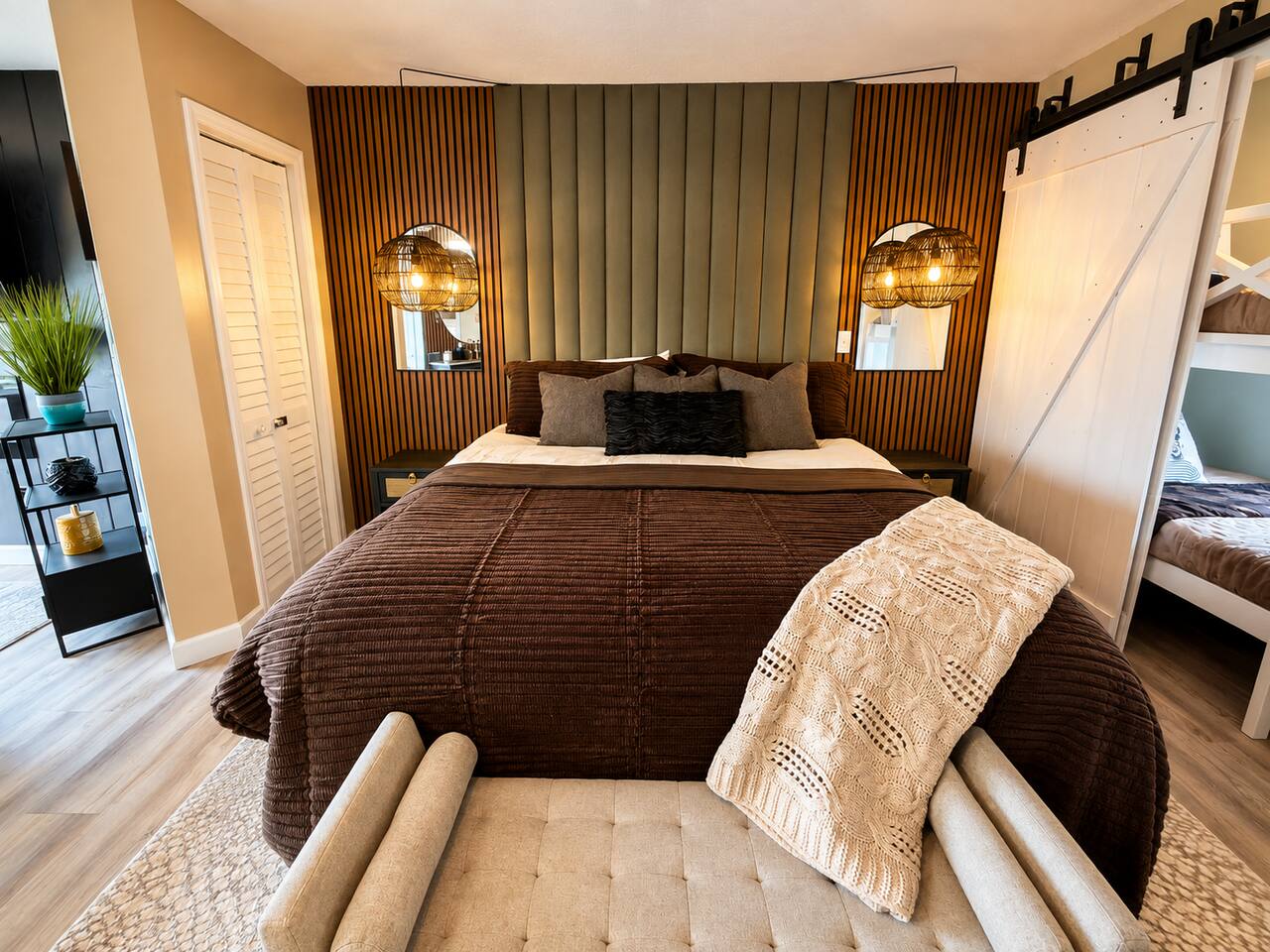 Unwind in this stylish king bedroom featuring warm wood accents, cozy neutral bedding, soft pendant lighting, and a comfortable sitting area. Thoughtful design and inviting textures create the perfect mountain retreat.