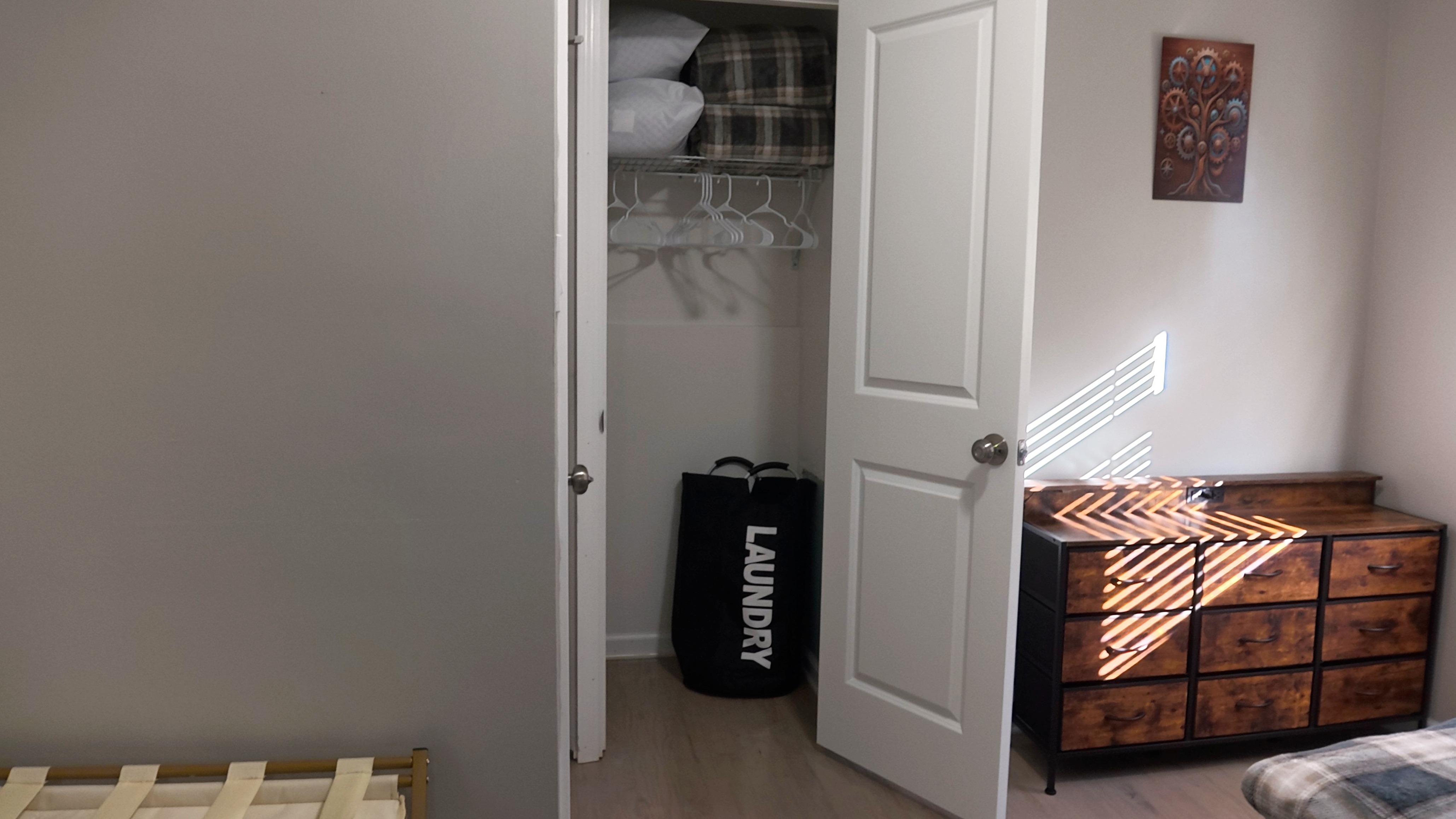 Bright bedroom corner with closet storage, extra linens, and dresser