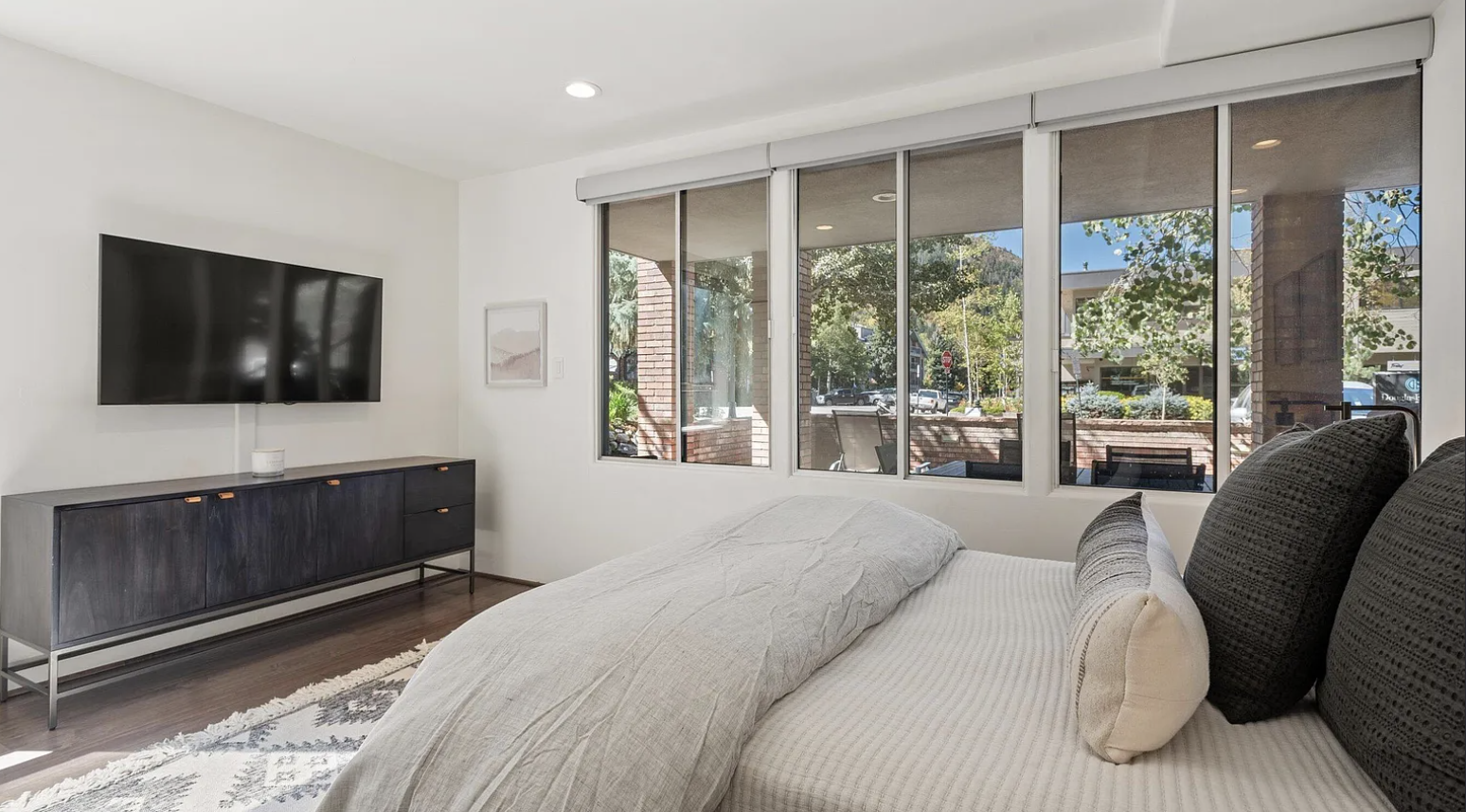Bright modern bedroom with large windows, TV, and serene outdoor views