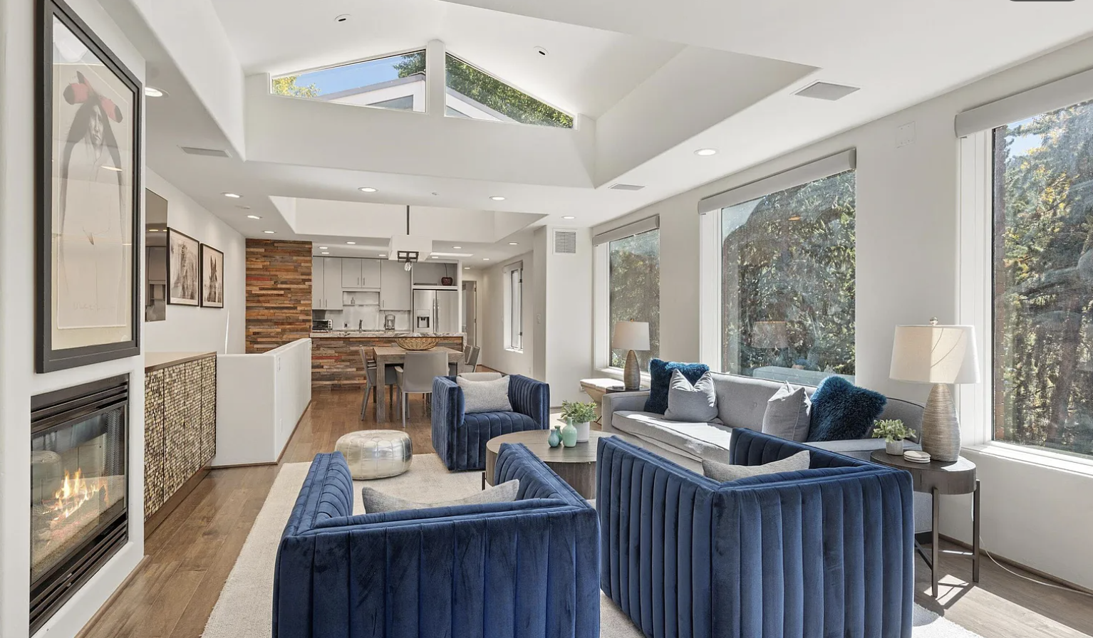 Sunlit modern great room with skylights, fireplace, and forest views