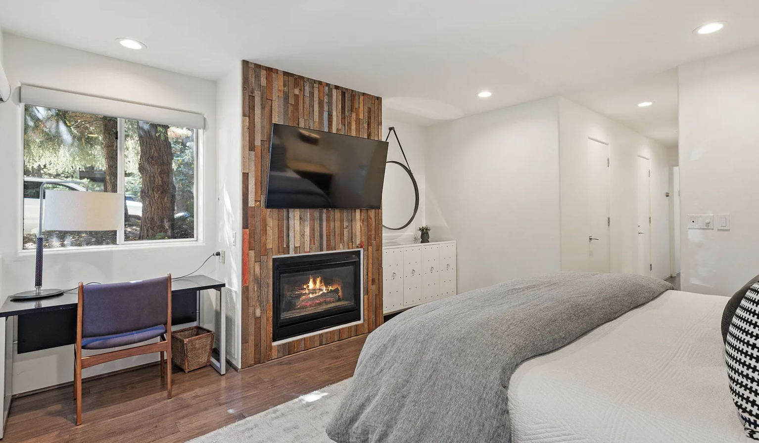 Modern bedroom with fireplace, TV, and bright workspace