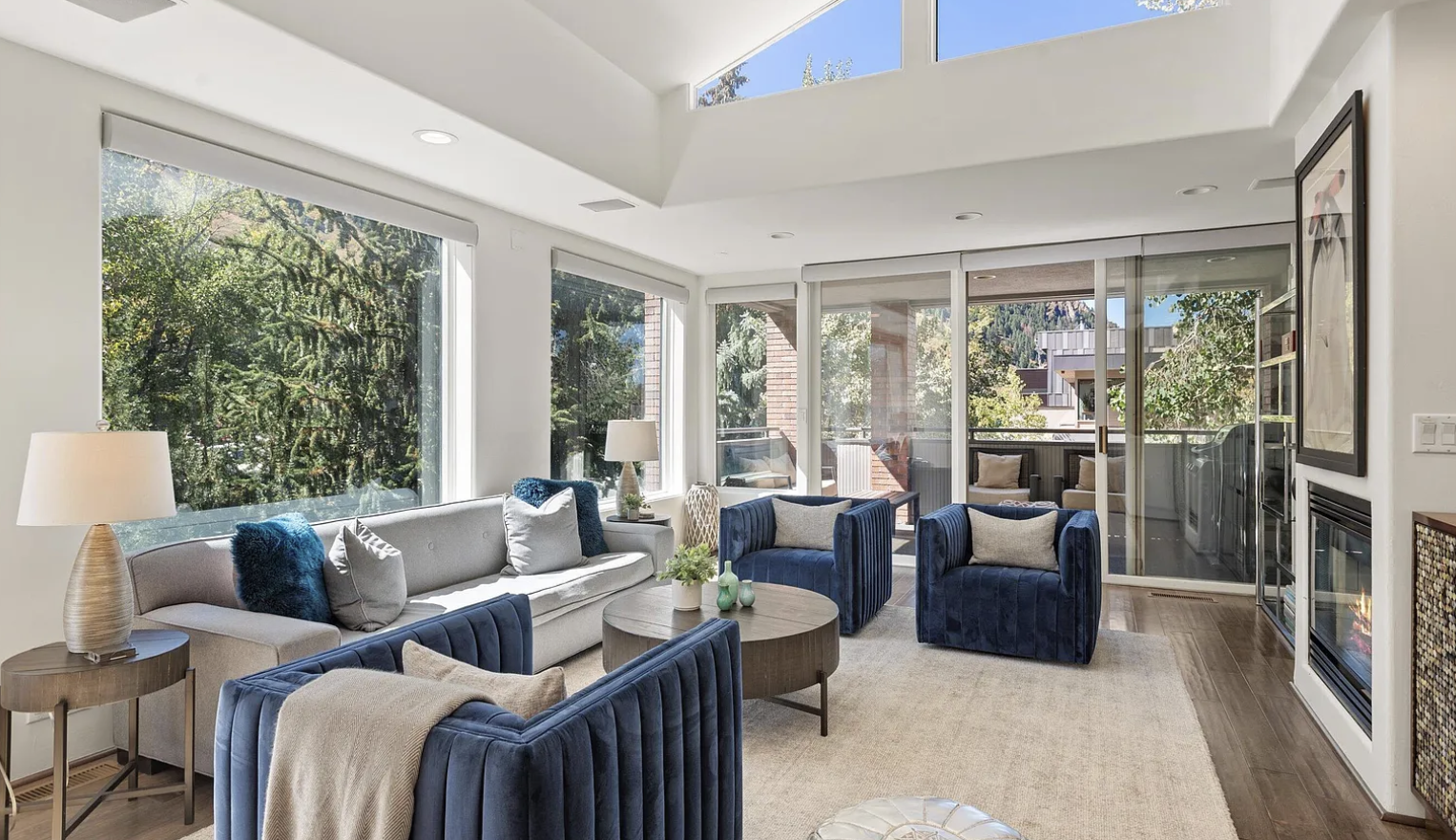 Sun-filled modern lounge with fireplace, large windows, and balcony access