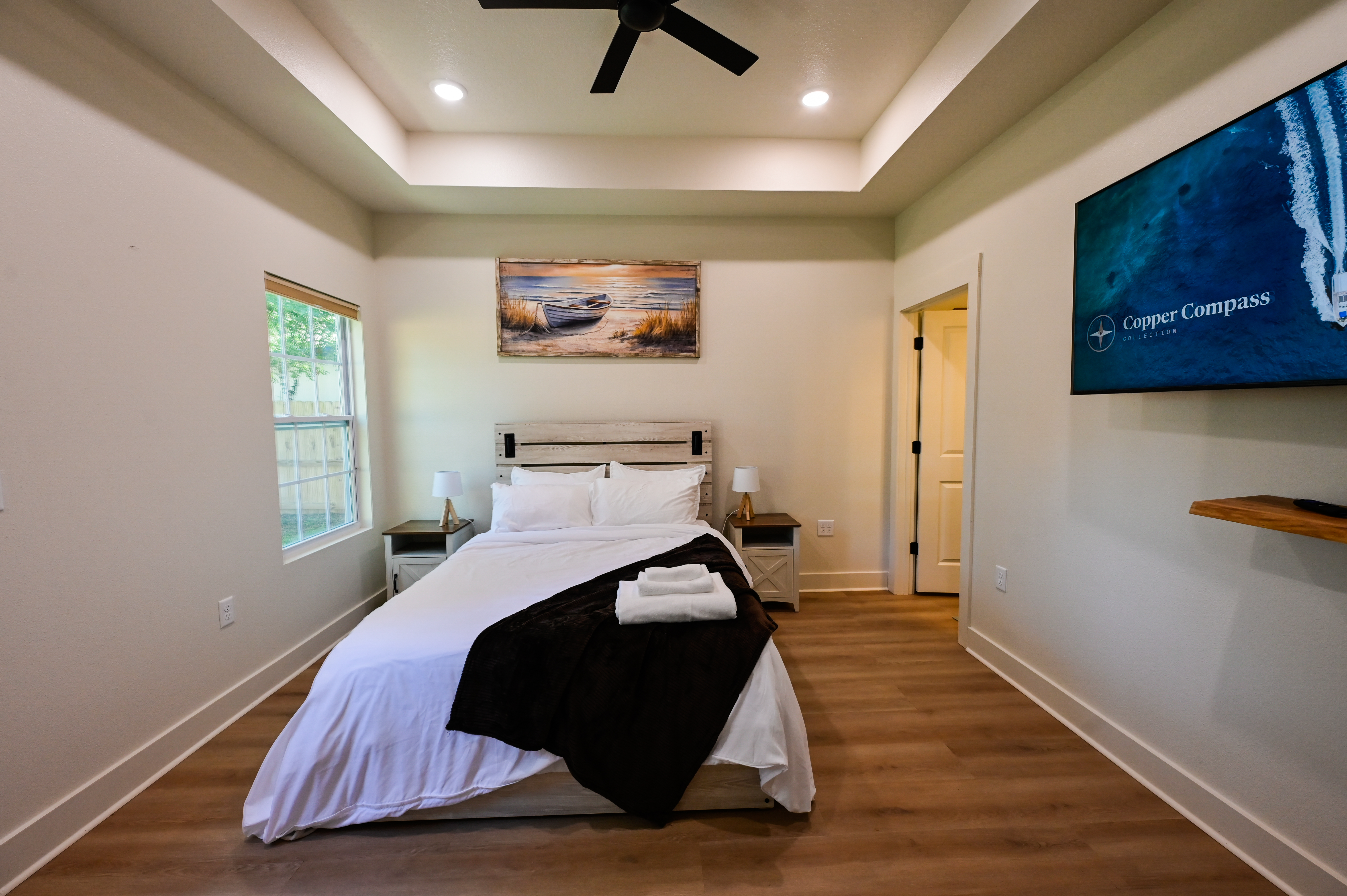 Bright modern bedroom with tray ceiling, TV, and cozy coastal style