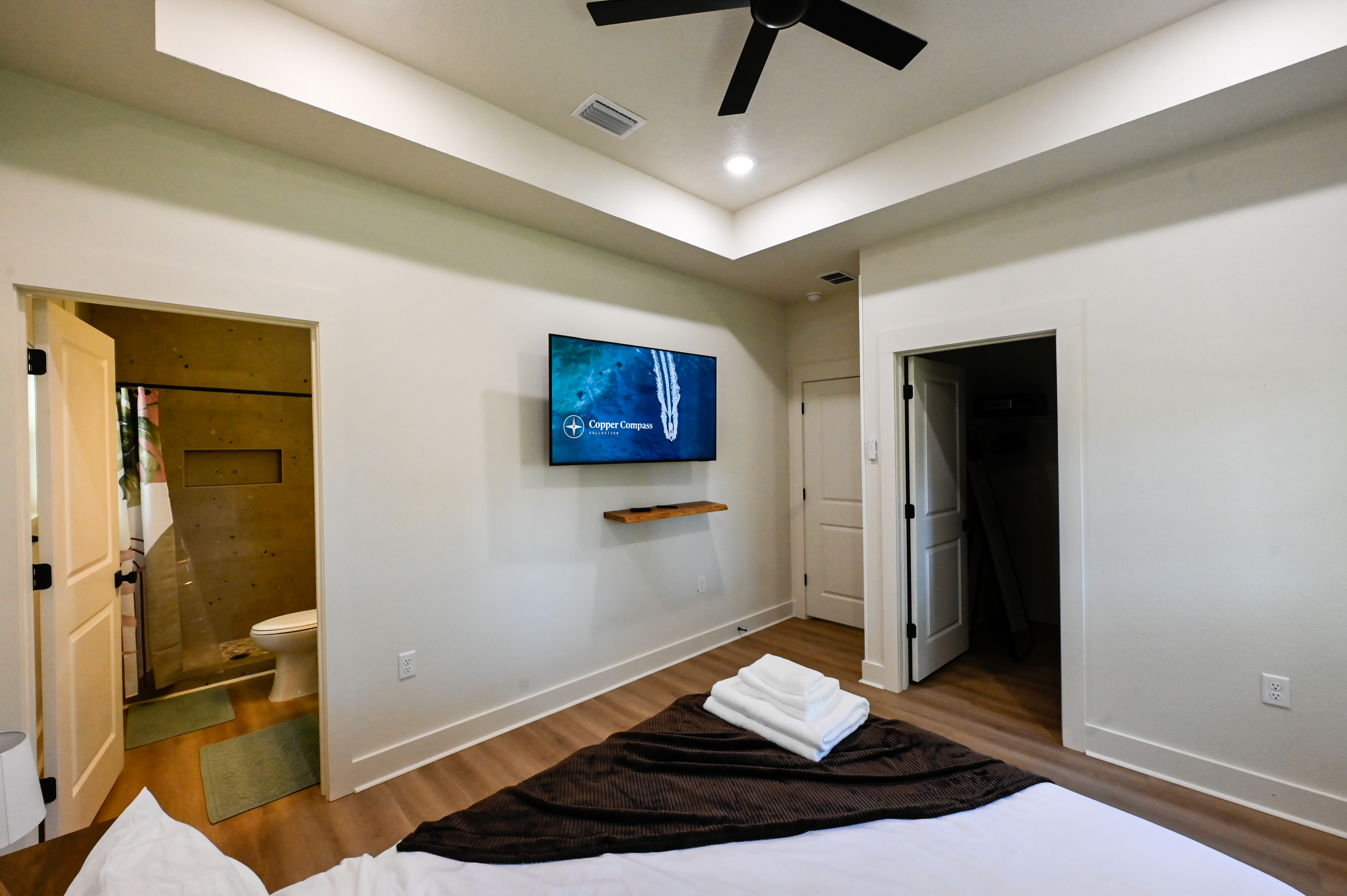 Modern bedroom with ensuite bath, tray ceiling, and wall-mounted TV