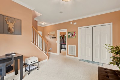 The office has a desk and printer on one side and a wide double closet on the other, with the staircase alongside. The black futon at the edge of the frame opens up into a bed if needed, and an open door leads through to a queen bedroom.