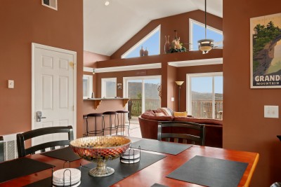 Placemats are set and the glass fruit bowl is out on the dining table, with the breakfast bar and its four stools right behind. The deck sliders sit just past the living room, so plates can go outside on a clear evening without a long walk.