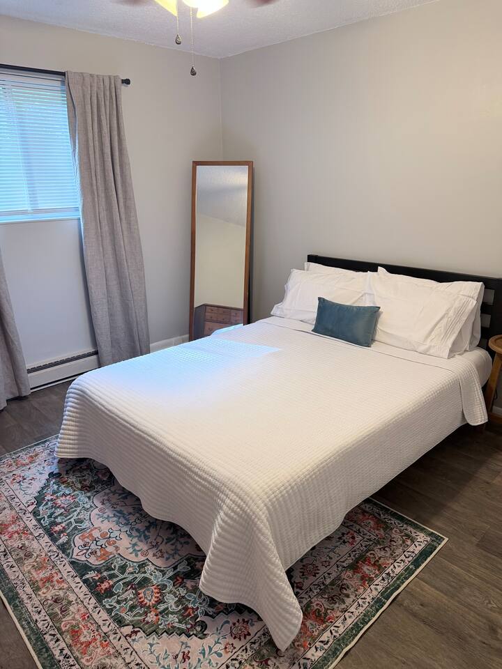 Queen bedroom with full-length mirror, bedside lighting and plenty of natural light
