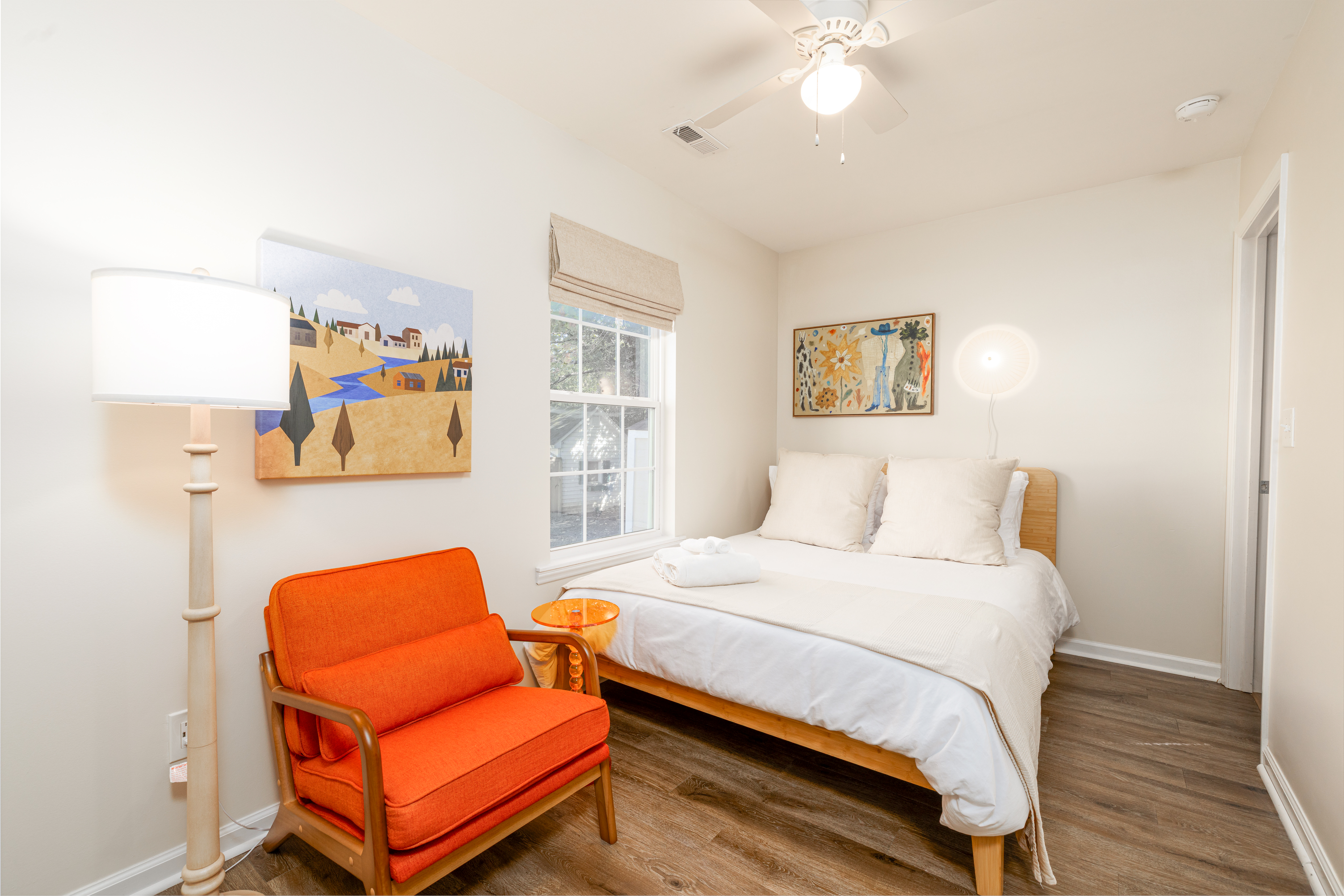 Primary bedroom with a queen bed, reading chair and blackout roman shade