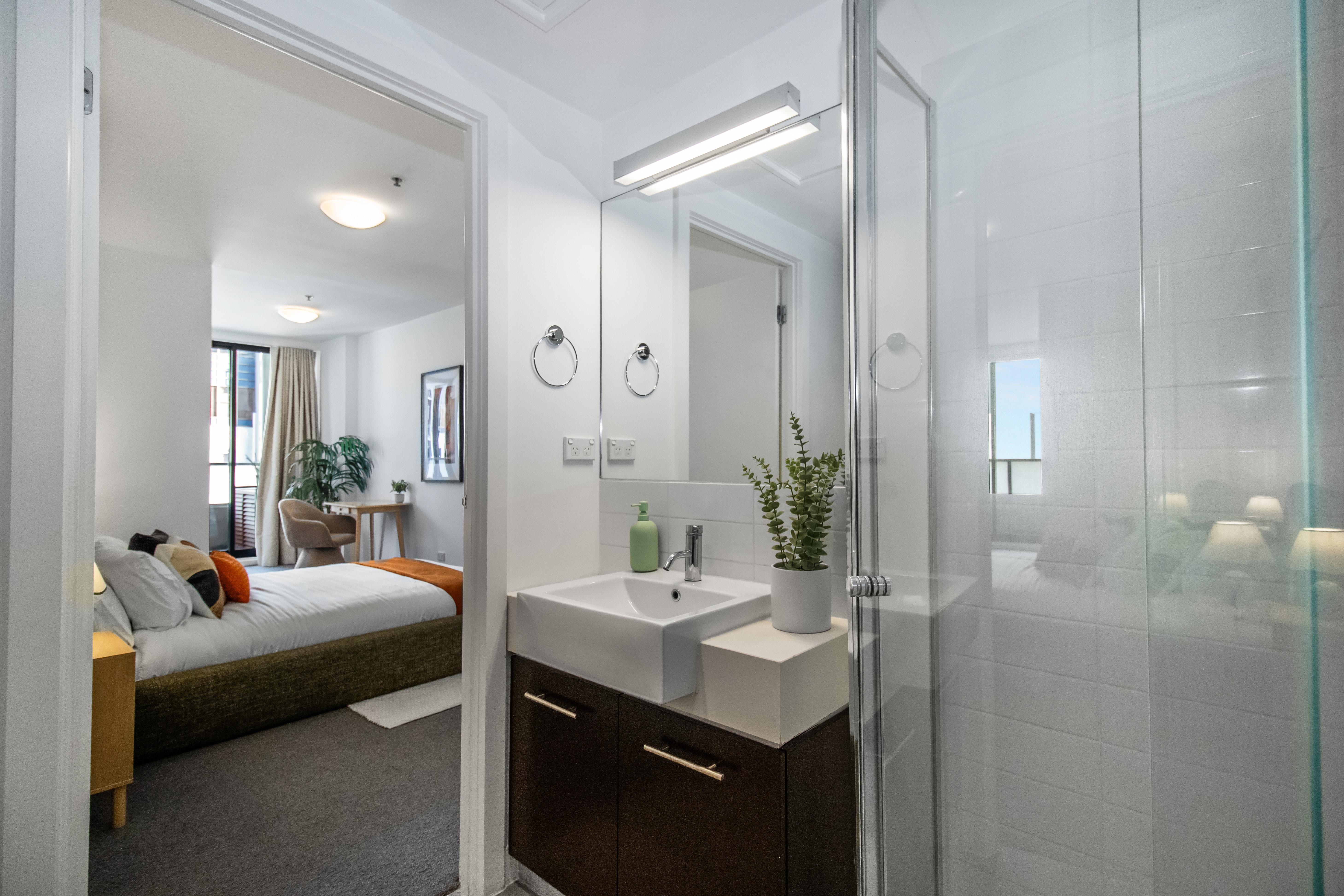 Bright modern bathroom with glass shower and adjoining cozy bedroom