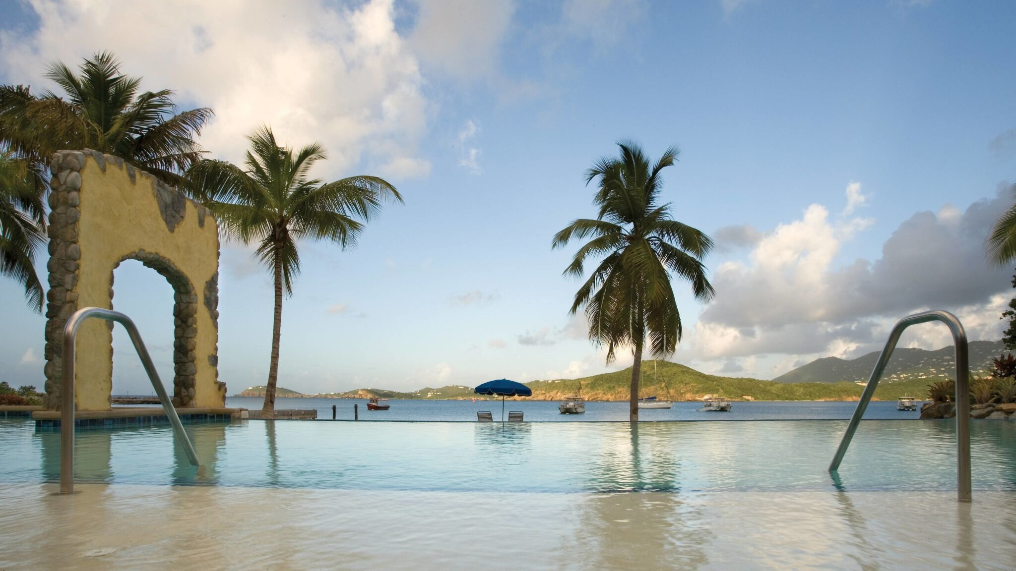 Waterfront infinity pool with palms, island views, and serene tropical charm