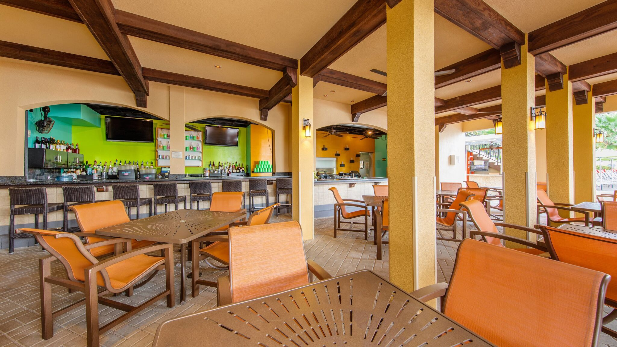 Covered open-air lounge with bar seating, TVs, and resort-style dining