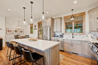 Bright gourmet kitchen with large island seating and modern farmhouse finishes. Four barstools pull up to the quartz island for coffee and pancakes, the stainless fridge and dishwasher sit close, and the dining table waits around the corner.