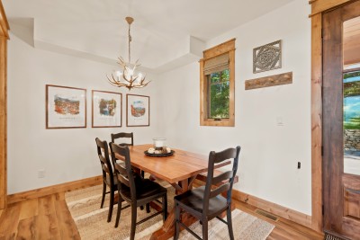Sunlit dining nook with four chairs plus a bench, so there is room for more than four, and warm natural light from the window. The trestle table sits by the front door under an antler chandelier, ready for quick breakfasts or long family dinners.