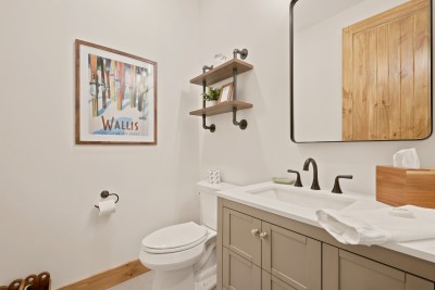 Bright modern bathroom with stylish vanity and warm wood accents. This main-level half bath sits just off the dining area, with pipe-and-wood shelves, a vintage Wallis ski poster on the wall and fresh hand towels stocked before every arrival.
