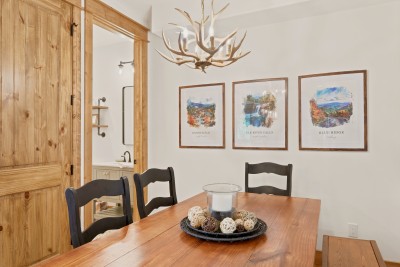Lodge-style dining space with wood finishes and statement antler chandelier. Gather around the plank-top table for family dinners, card games and lazy breakfasts, with watercolor prints of Banner Elk, Elk River Falls and the Blue Ridge on the wall.