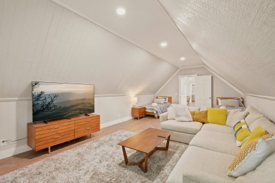 The movie room and lounge above the primary suite has a deep sectional, a large TV and twin beds tucked under the sloped ceiling, giving extra sleeping space for kids or teens. It is a second place to gather when the main living room fills up