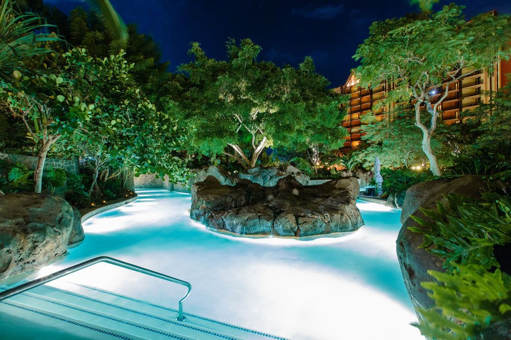 Tropical lagoon-style pool with glowing water and lush nighttime ambiance