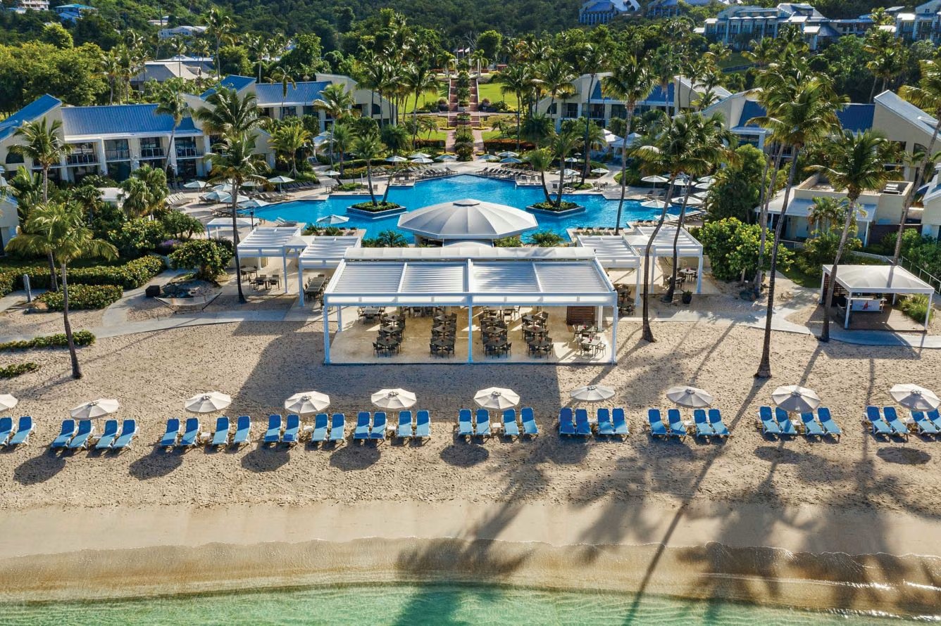 Beachfront resort with pool, palm-lined grounds, and relaxing lounge chairs