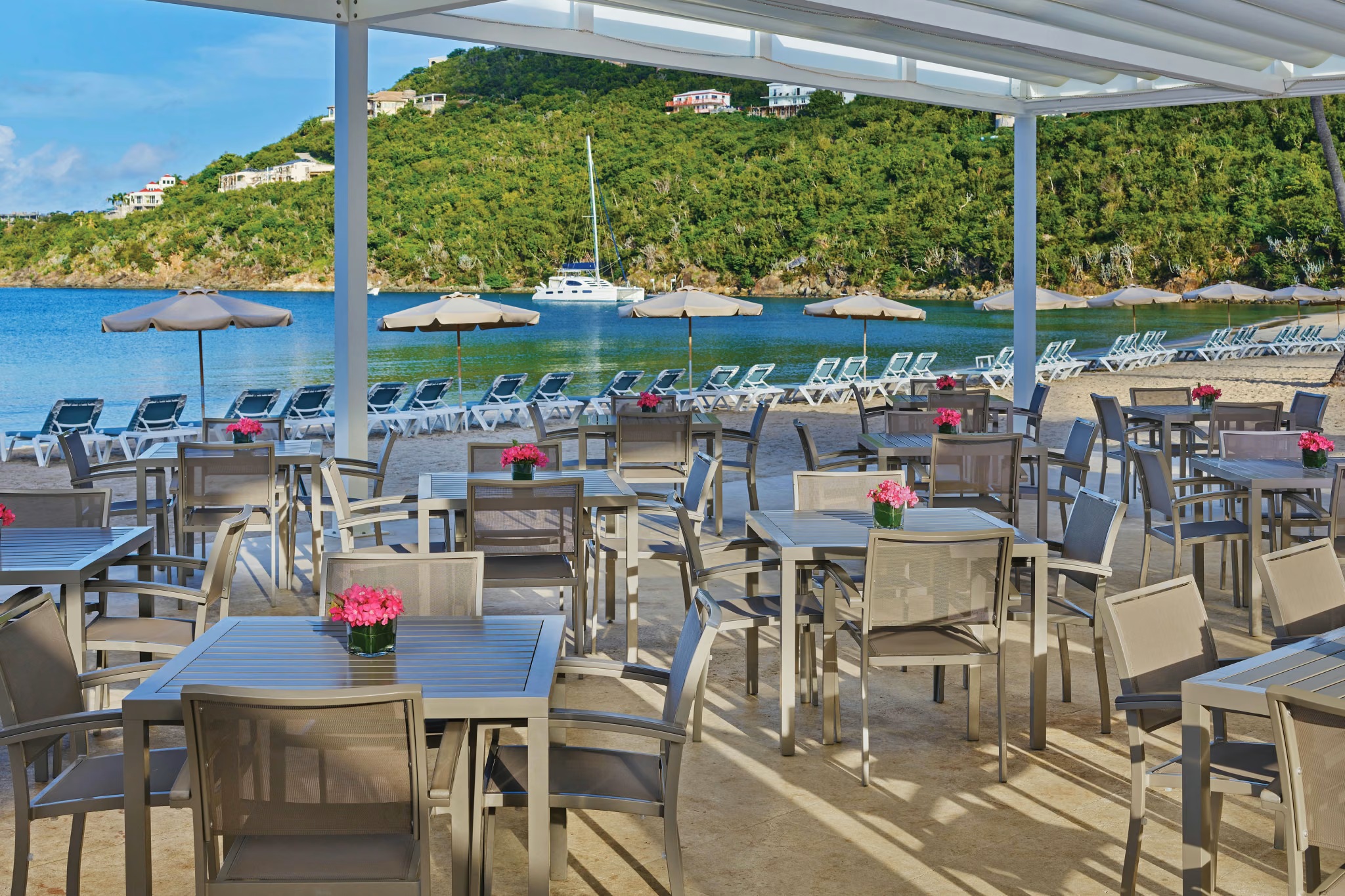 Beachfront dining terrace with ocean views, loungers, and a serene bay