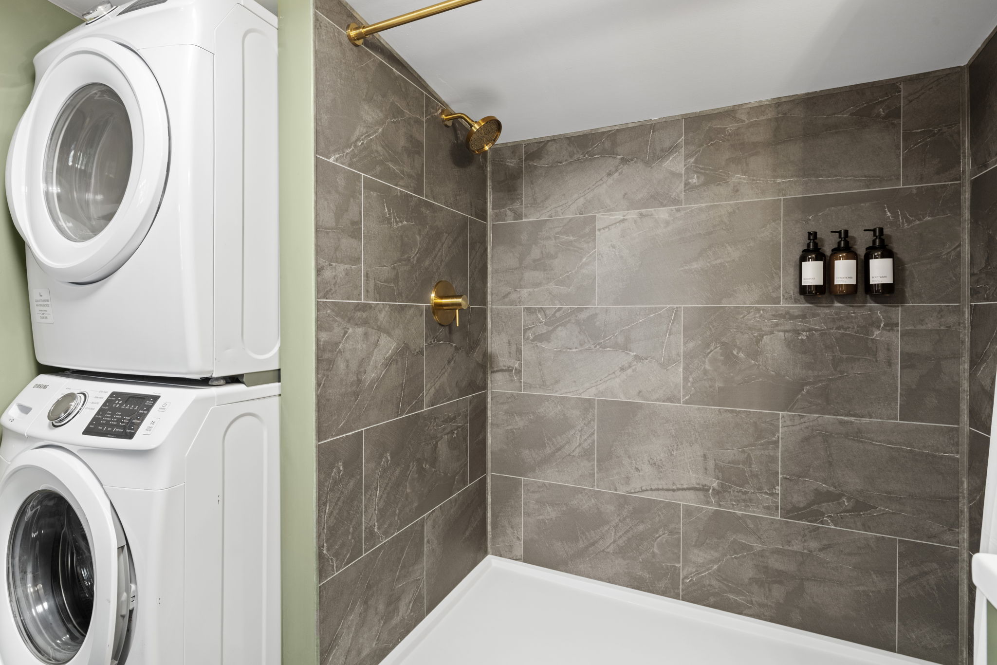 Modern tiled bath with brass fixtures and convenient in-unit laundry