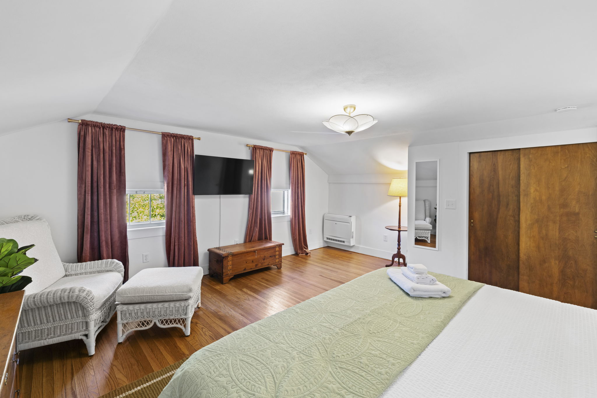 Spacious, sunlit bedroom with hardwood floors, TV, and cozy seating