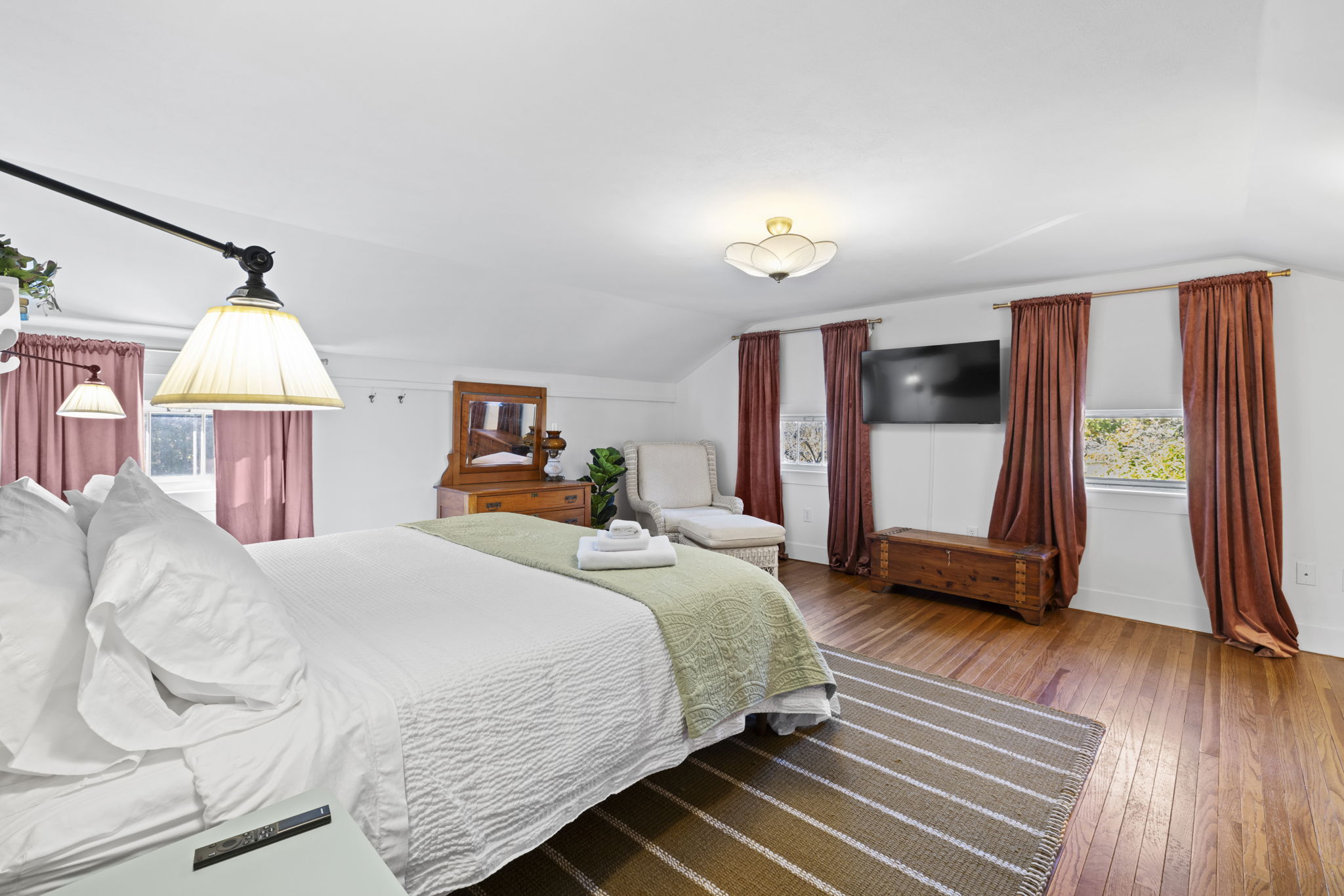 Spacious bedroom with hardwood floors, TV, and cozy lounge seating
