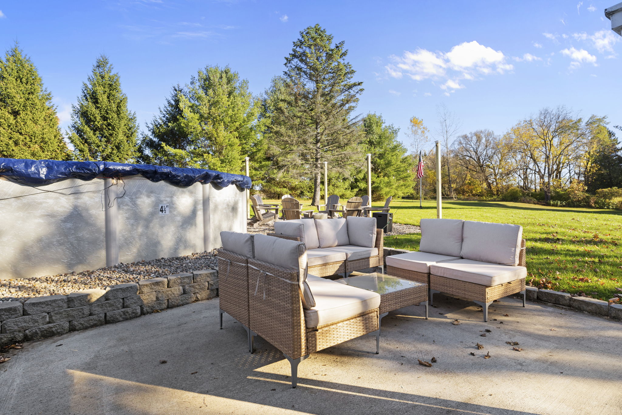 Sunny backyard patio with lounge seating, pool, and expansive green lawn