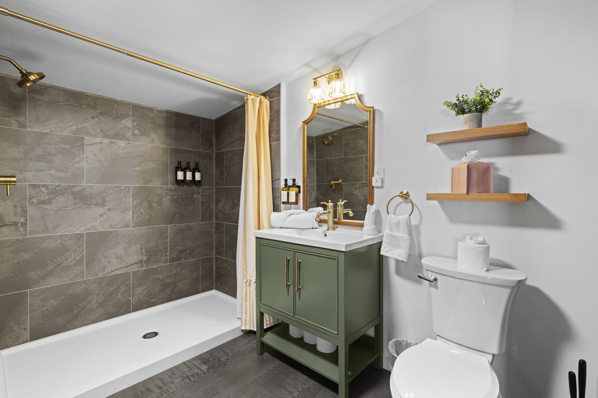 Stylish bath with walk-in shower, brass accents, and chic sage vanity