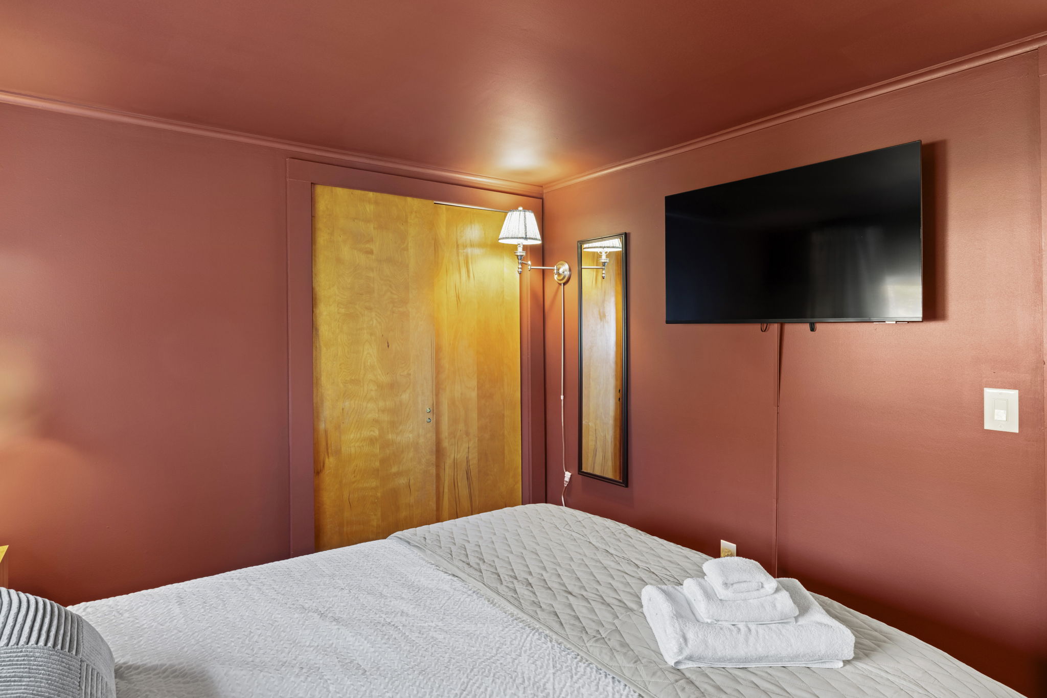 Cozy bedroom with wall-mounted TV, warm tones, and fresh towels