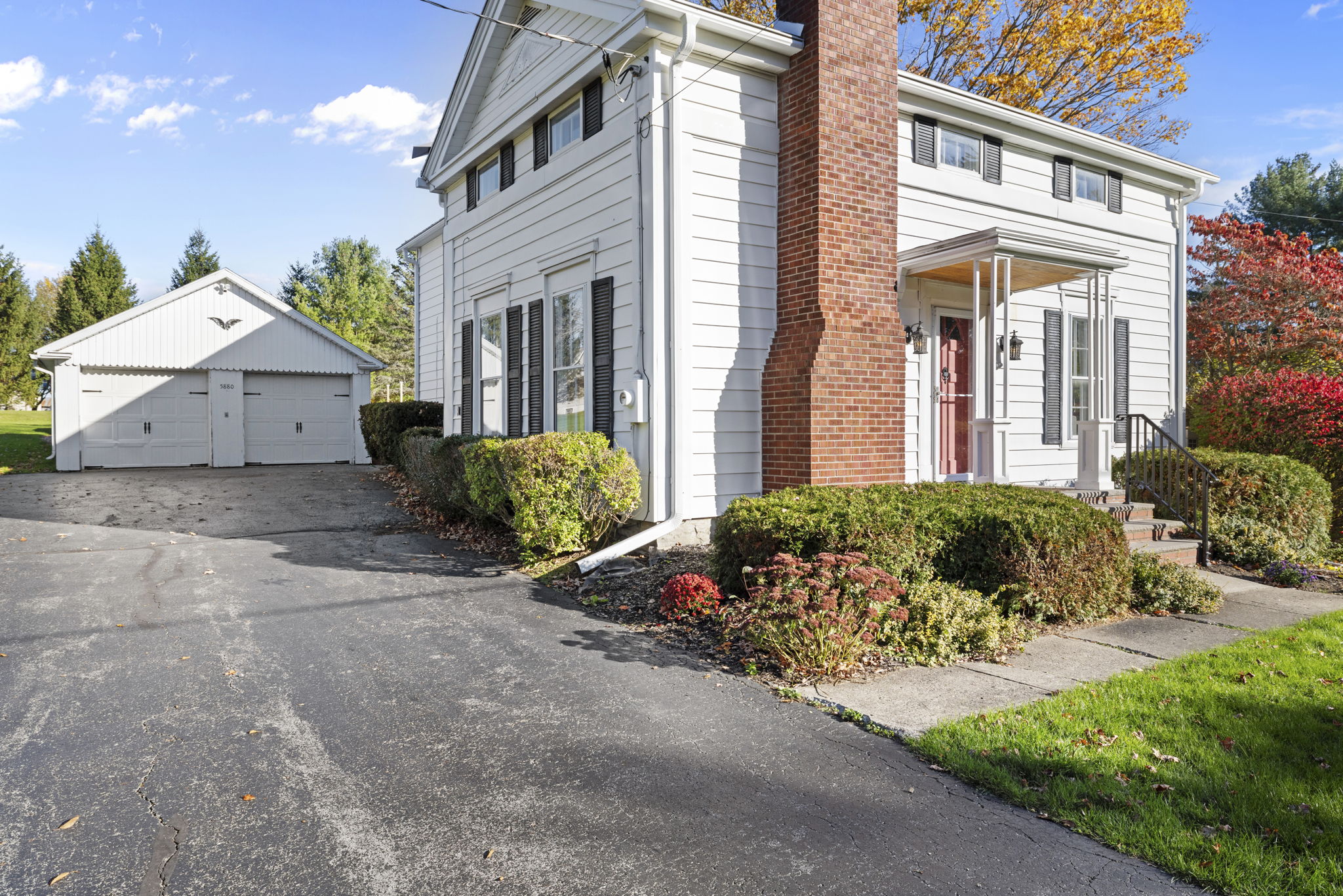 Charming white farmhouse exterior with detached garage and long driveway