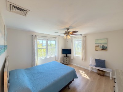 Bright sunlit bedroom with corner windows and a calm coastal feel