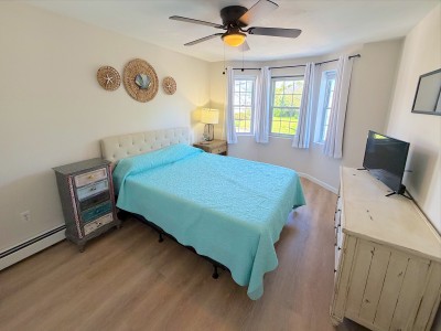 Bright coastal bedroom with queen bed, TV, and sunny windows