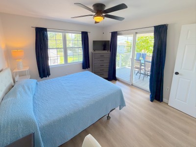 Bright bedroom with TV, ceiling fan, and private deck access