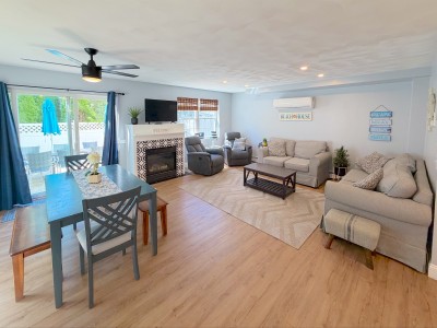 Bright coastal living area with fireplace, dining space, and patio access