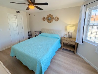 Bright coastal bedroom with natural light, ceiling fan, and cozy touches