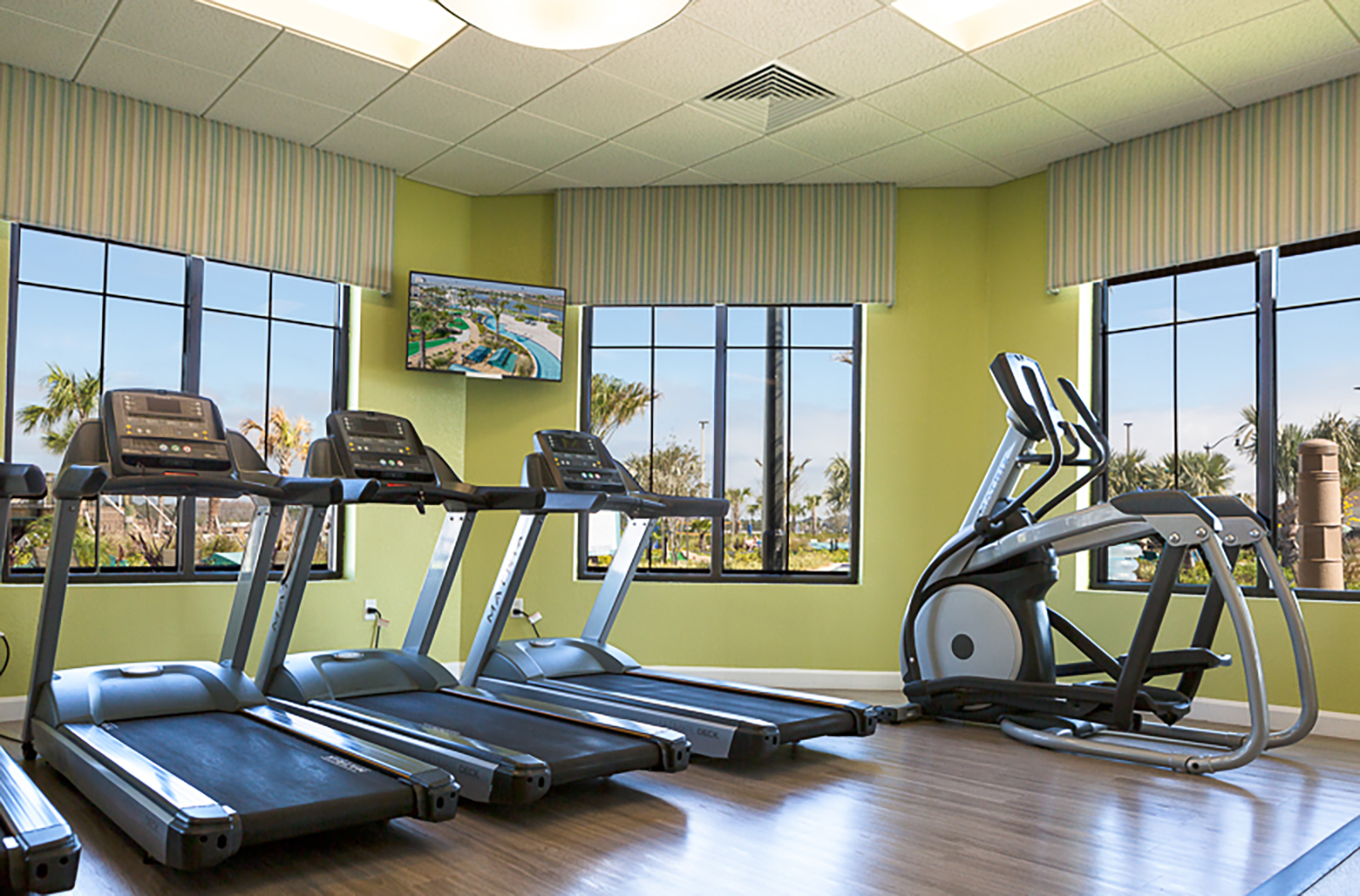 Bright on-site fitness room with treadmills, ellipticals, and sunny views