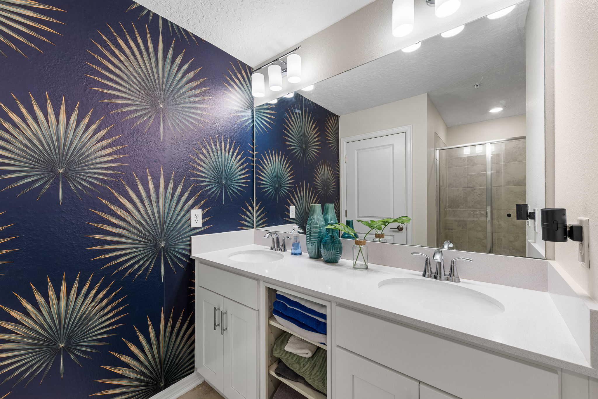 Stylish double vanity bath with bold designer wallpaper and glass shower