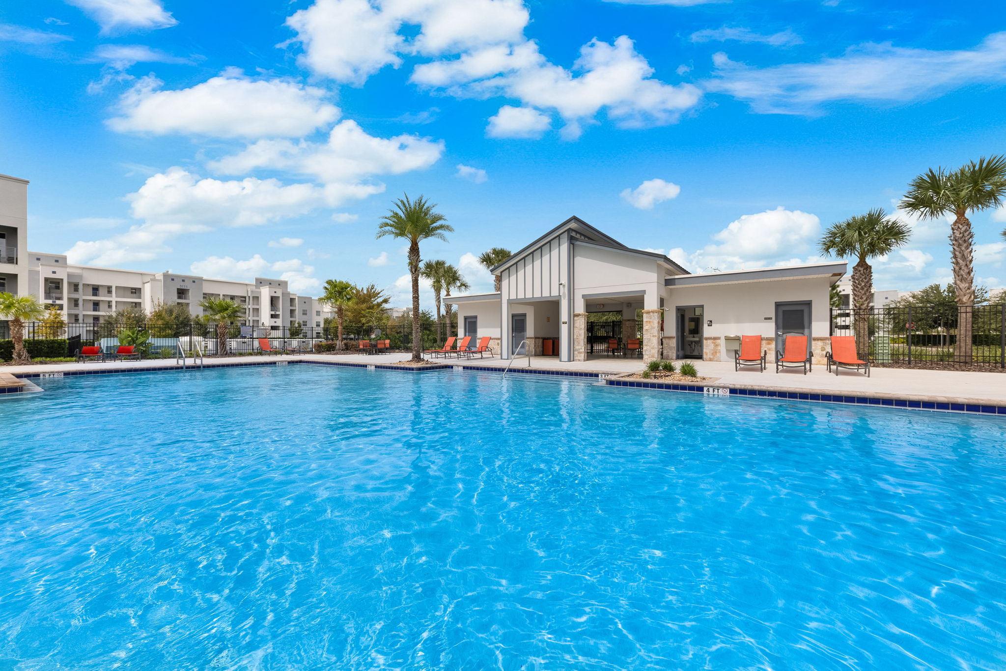 Resort-style pool with palm trees, loungers, and sunny clubhouse views