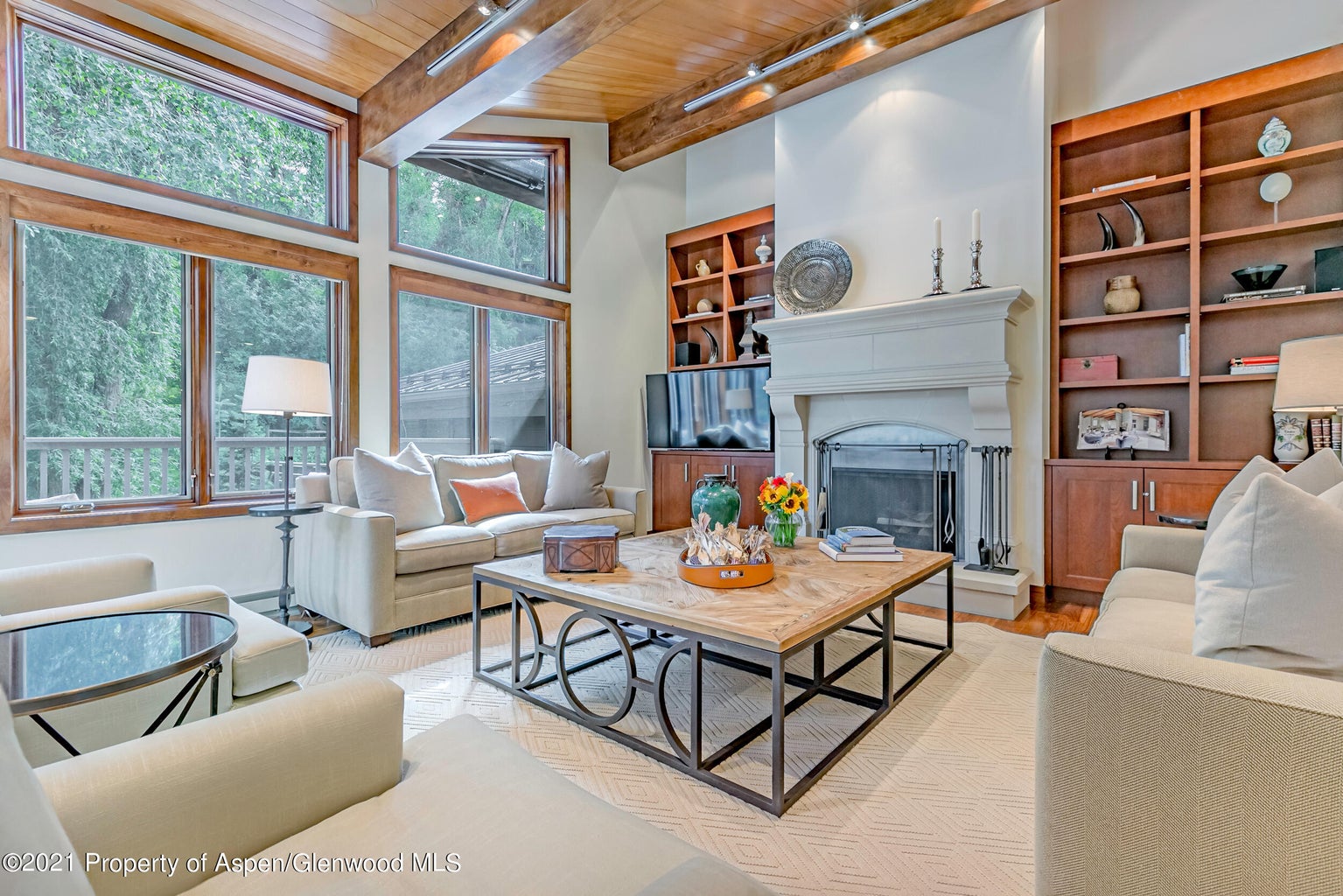 Sunlit living room with fireplace, vaulted ceilings, and forest views