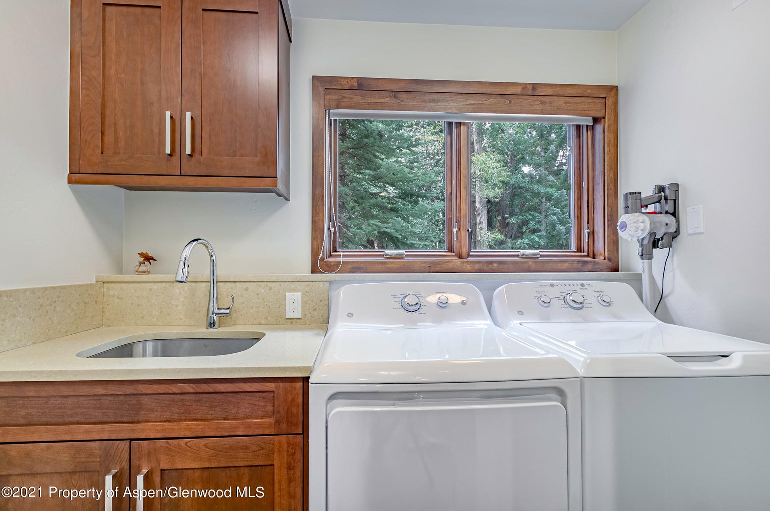 Bright laundry room with full-size washer/dryer, sink, and wooded view