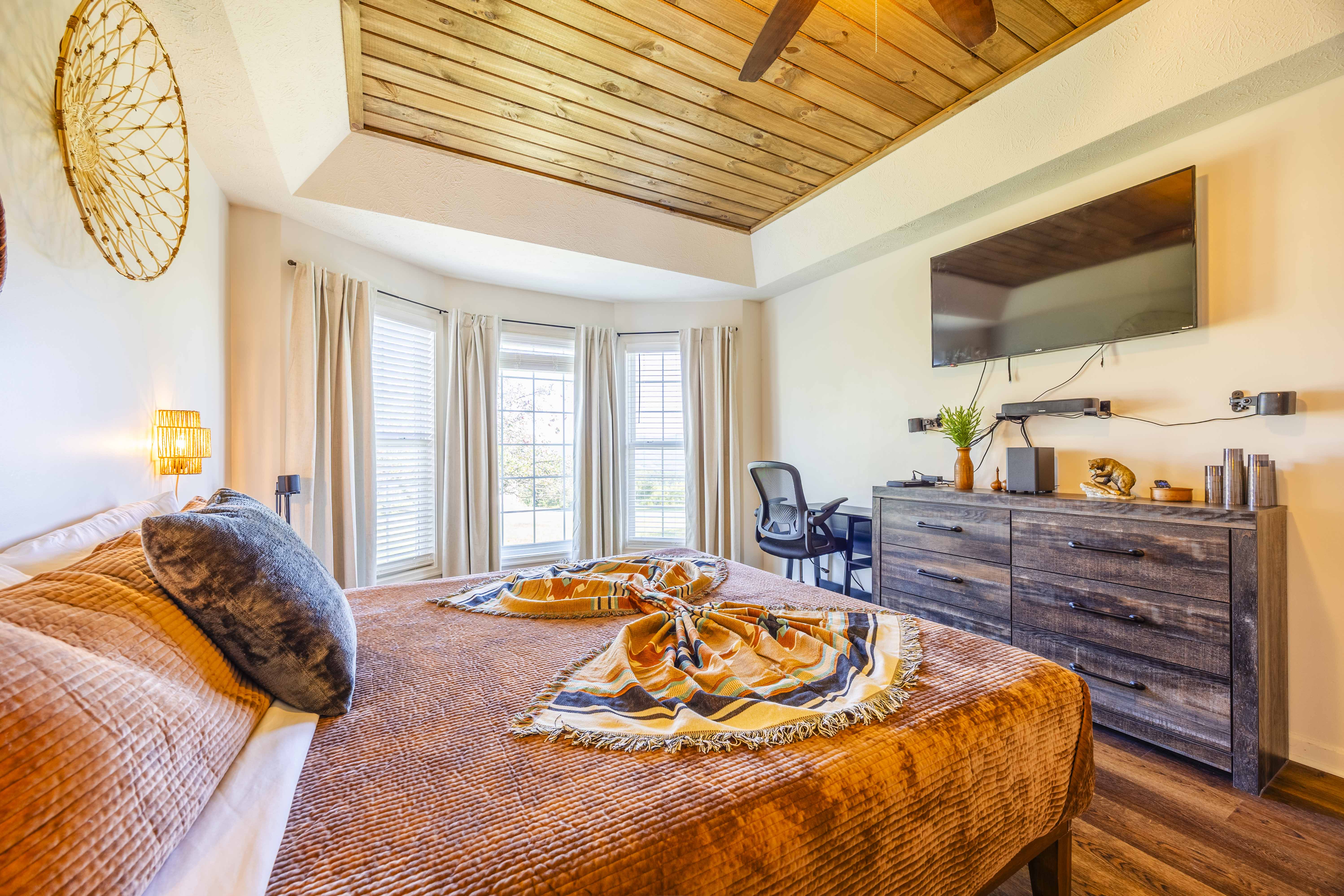 Bright, stylish bedroom with bay windows, TV, desk, and wood-accent ceiling