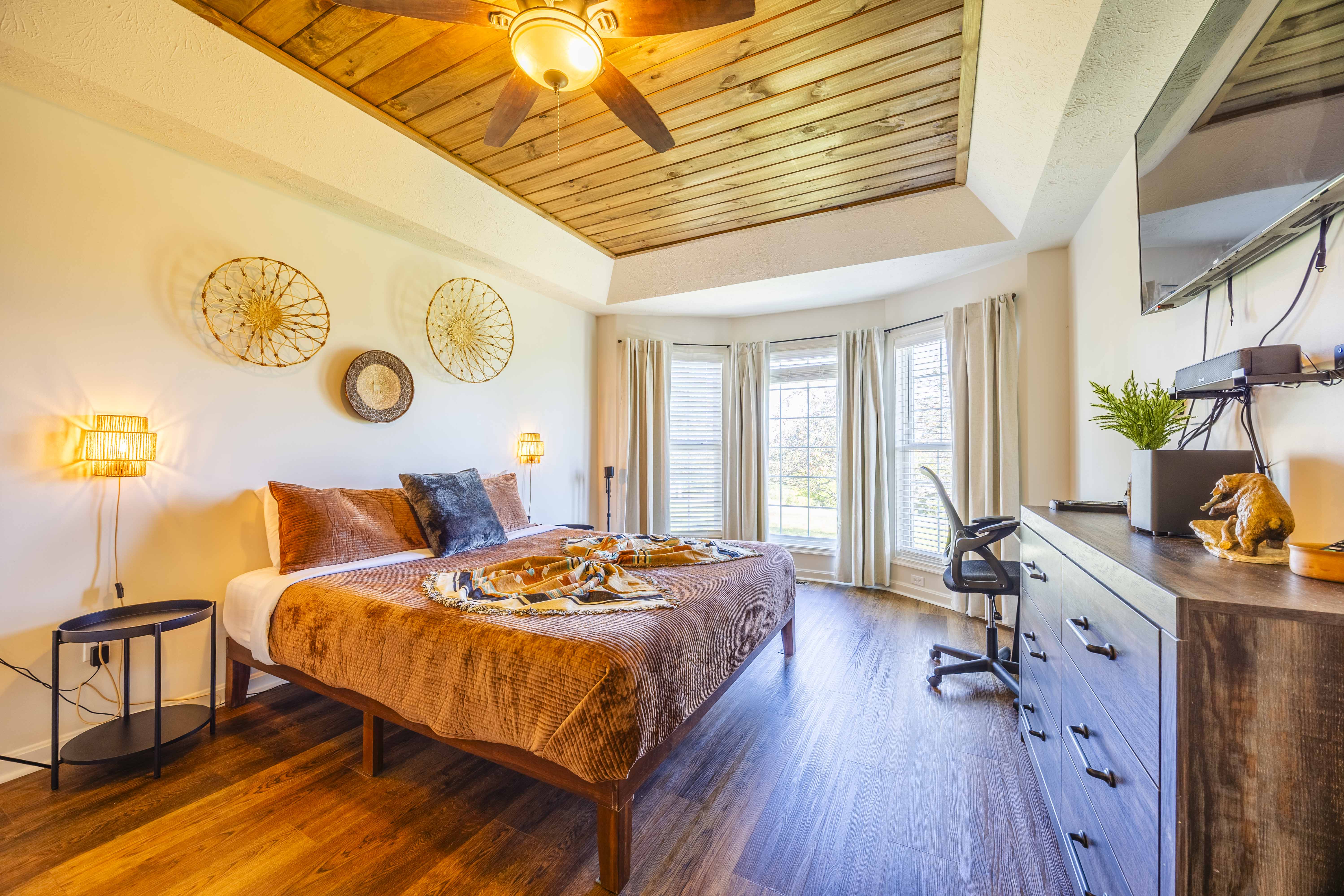 Bright rustic bedroom with bay windows, workspace, and cozy king bed