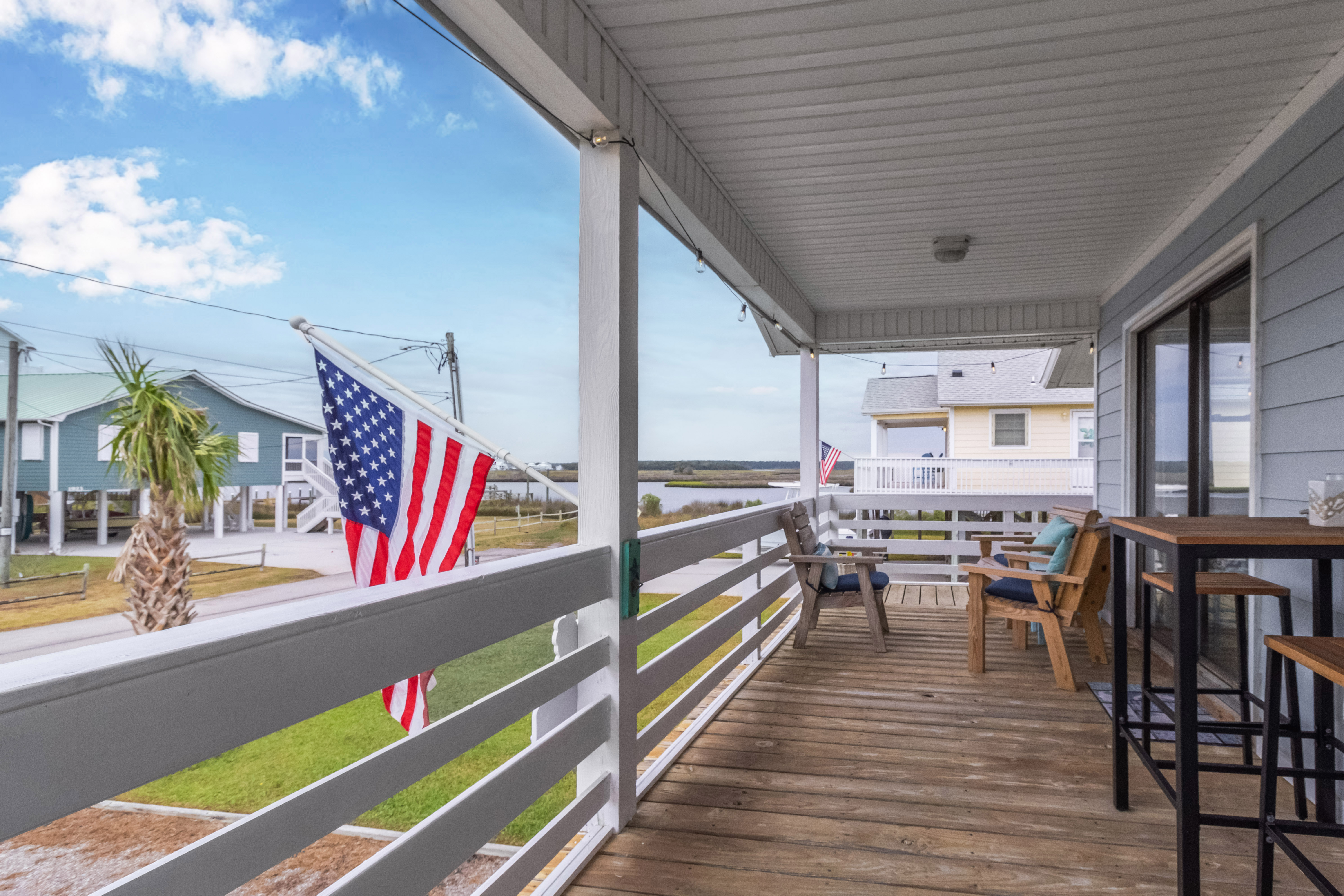 Covered coastal balcony with seating, dining space, and water views