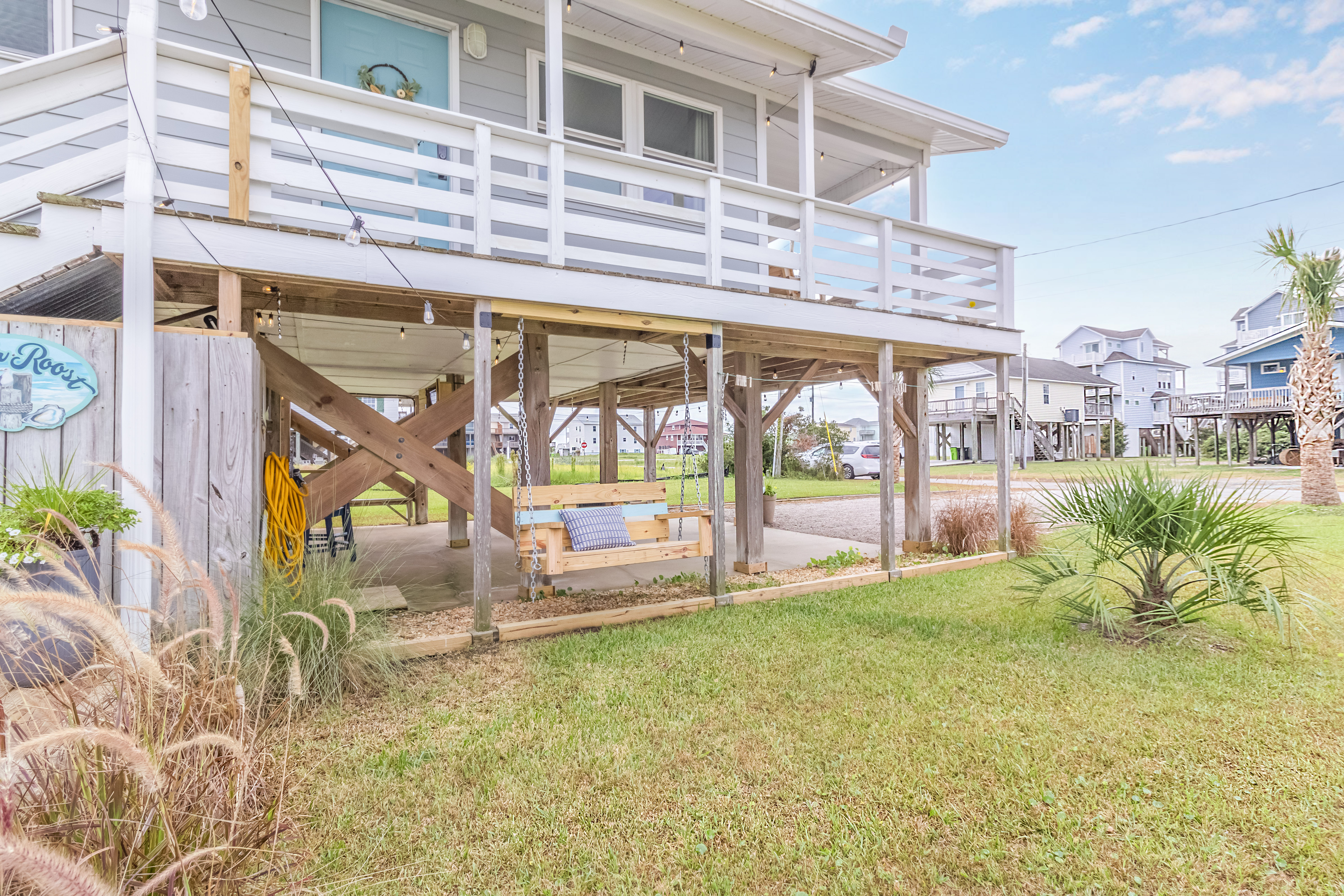 Raised beach home with wraparound deck, porch swing, and sunny yard