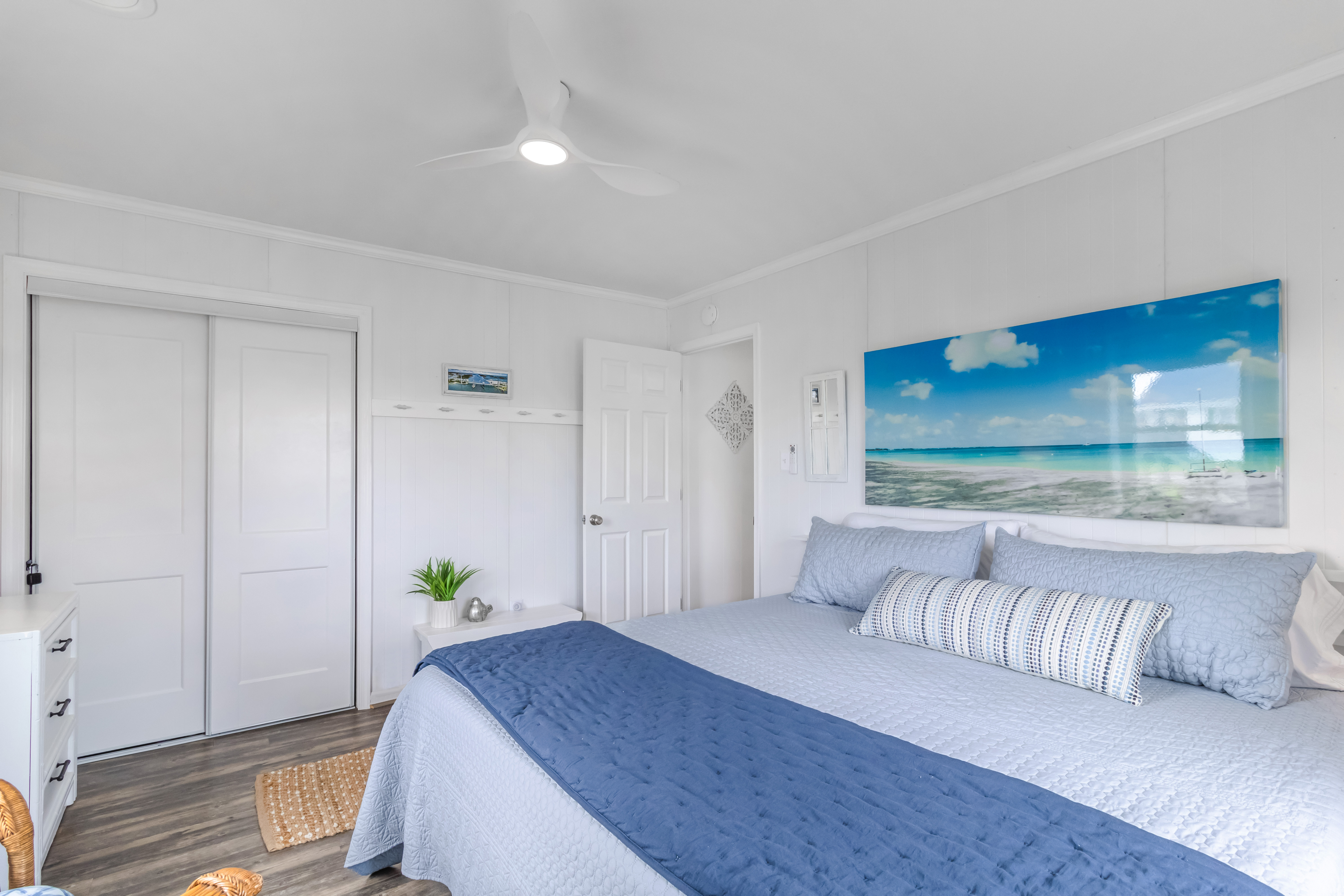 Bright coastal bedroom with king bed, beach art, and a calm airy feel