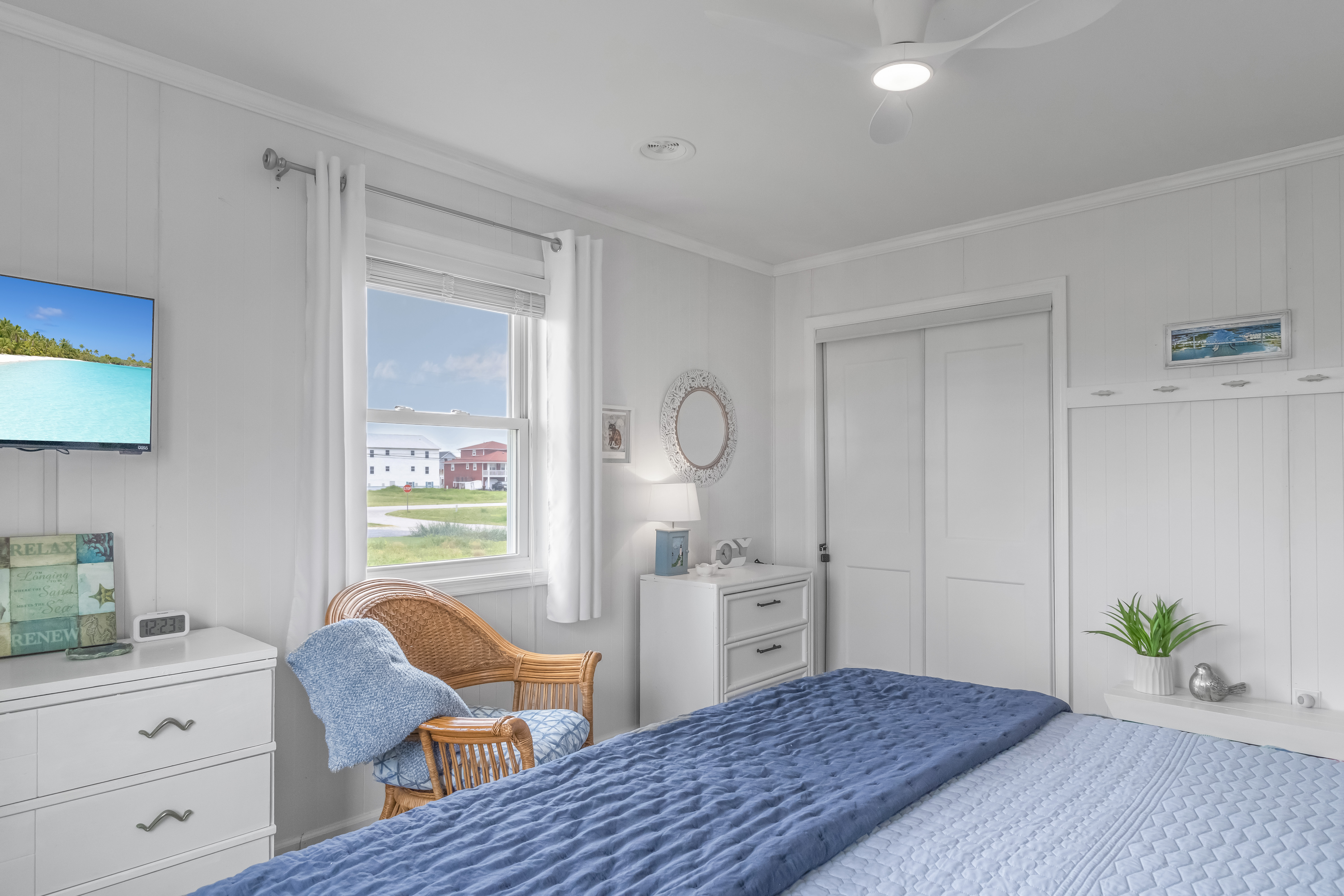 Bright coastal bedroom with TV, wicker chair, and serene blue accents